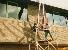 Lifting the Siskin House watermark panel into position to be fixed on the wall.